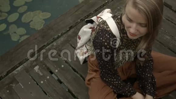 年轻女子坐在木墩上的湖边视频的预览图