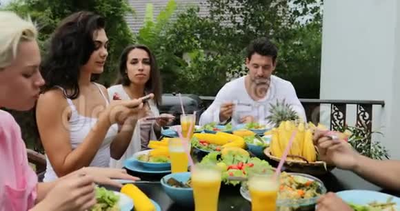 健康素食朋友交流坐在热带露台上的餐桌视频的预览图