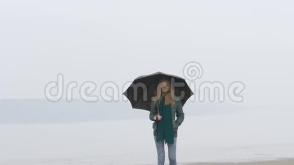 带着雨伞的女孩走向沙滩上的摄像机笑了起来关闭视频的预览图