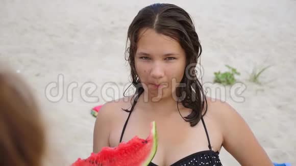 小朋友在沙滩上吃西瓜慢动作视频女孩少年长着粉刺吃西瓜概念视频的预览图