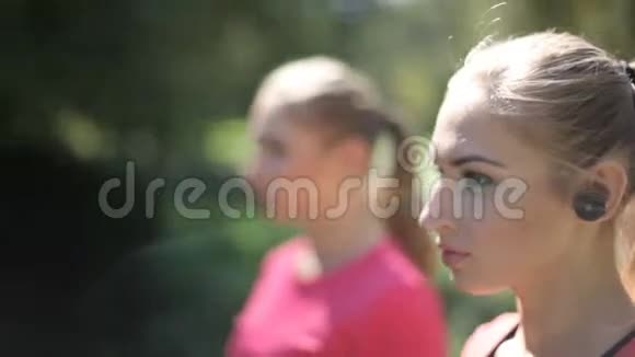 两个带无线耳机的女孩在公园里从事体育活动现代技术的优势视频的预览图