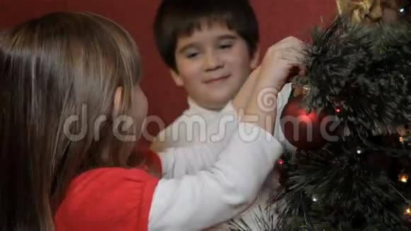 小男孩把装饰蝴蝶结挂在圣诞树上视频的预览图