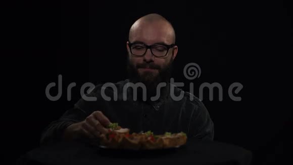 饥饿的男人在黑色背景上吃三明治视频的预览图