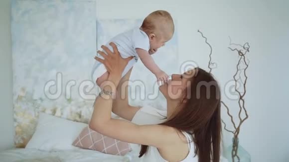 年轻可爱的女孩在床上和儿子玩一位年轻的母亲正在床上玩一个婴儿视频的预览图