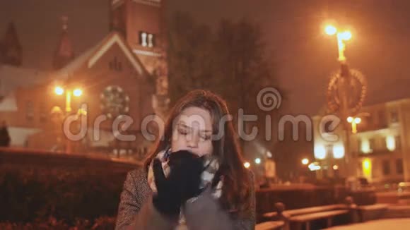 晚城背景下的一个年轻女孩温暖了双手在城市的灯光下下雪视频的预览图