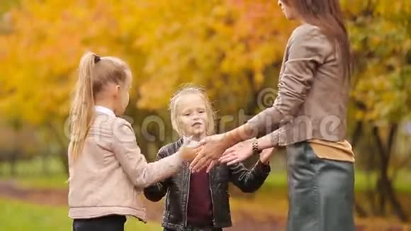 年轻的母亲和她的两个小女儿在秋公园玩游戏视频的预览图