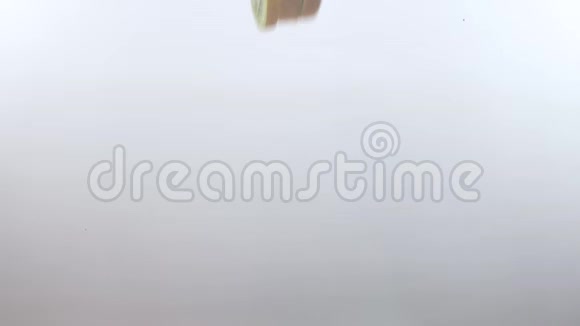 猕猴桃片在白色背景下慢慢落入清澈的水中视频的预览图