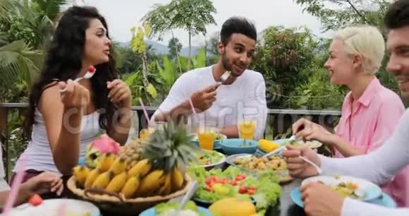健康素食朋友交流坐在热带露台上的餐桌视频的预览图