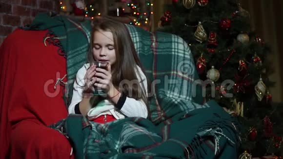 在圣诞树附近用毯子包着喝茶的特写女郎视频的预览图