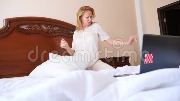 穿着睡衣的女人从笔记本电脑传来的欢乐的消息在床上欢快地跳舞4k慢动作视频的预览图