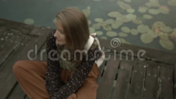 年轻女子坐在木墩上的湖边视频的预览图