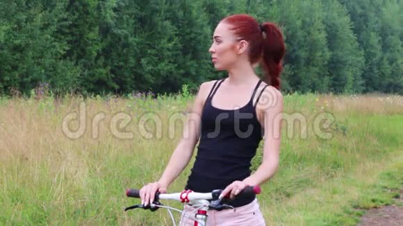 漂亮的年轻女子骑着自行车站着夏天在户外看视频的预览图