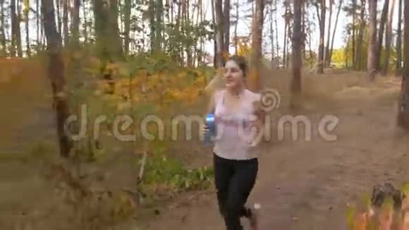 在森林里慢跑时一张美丽的年轻女子喝水的照片视频的预览图
