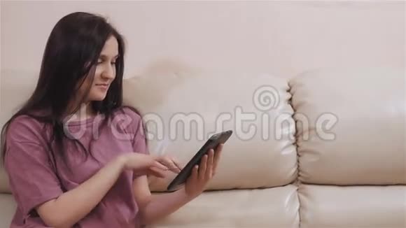 年轻的布鲁内特女孩在皮革沙发在家和工作在餐桌上视频的预览图