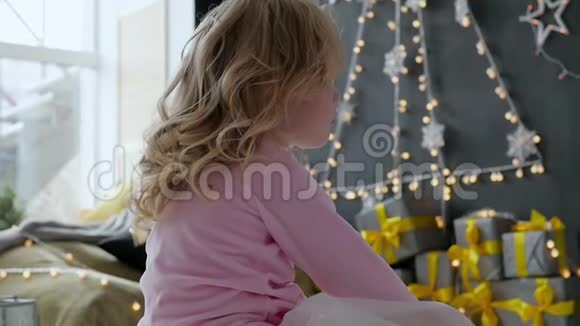 女孩坐在房子的地板上拿着圣诞礼物和花环女孩坐在后面视频的预览图