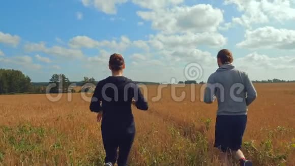 一个年轻人和一个穿着运动服的女孩正沿着一个谷物场跑步视频的预览图