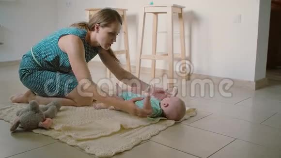 一位美丽的年轻母亲抬起她可爱的微笑婴儿帮助他站起来慢动作视频的预览图