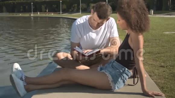 浪漫的一对夫妇在夏天的公园里在水边看书放松视频的预览图