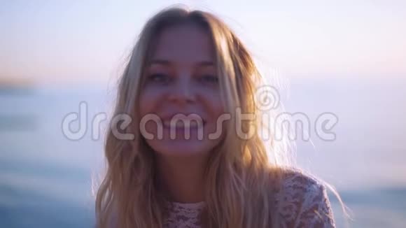 一个年轻的女孩对着镜头微笑太阳在她身后而在海边视频的预览图