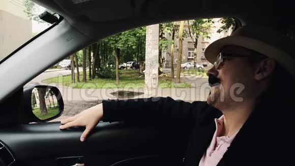 有胡子的人穿着晚餐夹克帽子眼镜坐在车里唱歌夏季视频的预览图