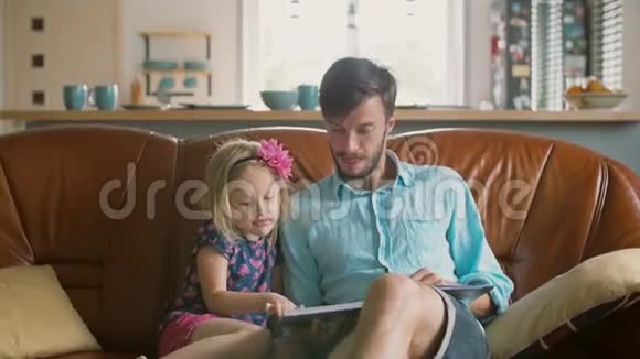 金发小女孩正在选择一个故事她慈爱的父亲将在沙发上阅读慢动作视频的预览图