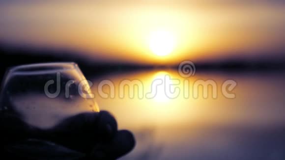 在日落和湖边的背景下浪漫的夜晚用玻璃杯检查饮料慢动作视频的预览图