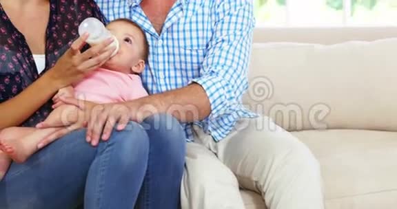 可爱的一对夫妇坐在沙发上给他们的孩子喂食奶瓶视频的预览图