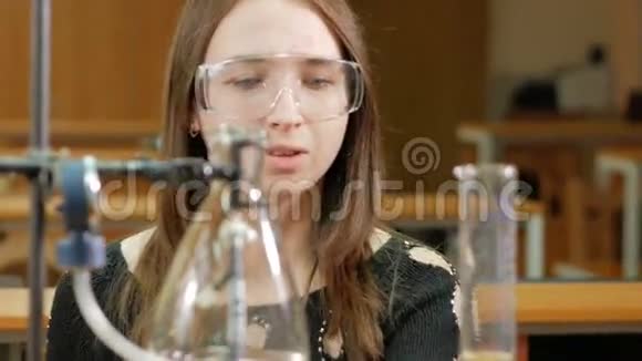 年轻的女学生从事化学工作并在大学里写出结果安全眼镜无外袍烧杯和视频的预览图