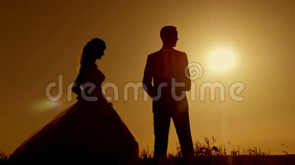 新娘和新郎的剪影在美丽的橙红色晚霞中亲吻视频的预览图