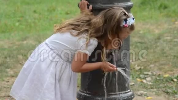 在炎热的夏天穿着一件连衣裙的小可爱的女婴从罗马喷泉里喝水视频的预览图