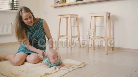 美丽的母亲正在帮助她的孩子学习如何在厨房地板上的毯子上爬行慢节奏视频的预览图