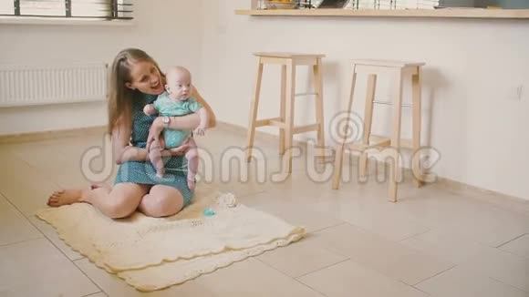 美丽的母亲抱着她珍贵的孩子坐在厨房的地板上微笑和他说话慢节奏视频的预览图