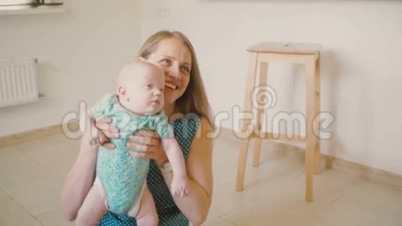 年轻的母亲正在举起她珍贵的婴儿坐在厨房的地板上微笑着和他说话视频的预览图
