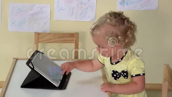 可爱的女婴用平板电脑坐在小桌旁视频的预览图