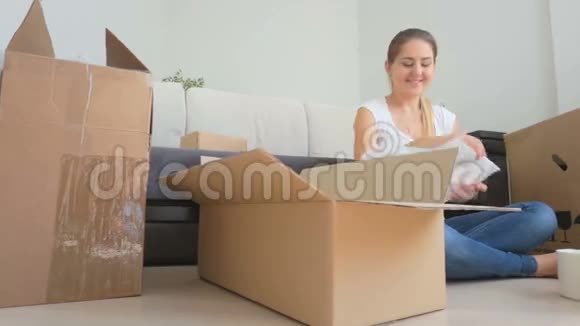 年轻女子坐在地板上用纸板箱包装花瓶和杯子视频的预览图