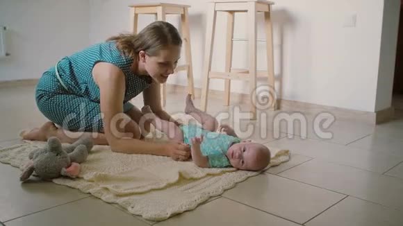 一位美丽的年轻母亲正看着她的儿子他躺在厨房地板上的毯子上慢节奏视频的预览图