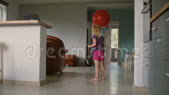 一个女孩和她父亲在客厅里玩一个大红色健身房气球的背部慢动作视频的预览图