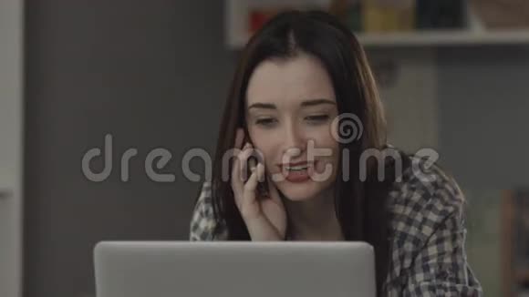 快乐的年轻女人手提电脑躺在床上在电话里说话视频的预览图