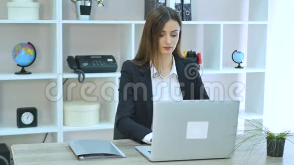 侧视商务女性在电话交谈坐在桌旁办公室里放着笔记本电脑视频的预览图