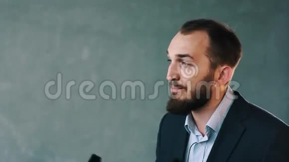 穿着夹克和条纹衬衫的大胡子男人热情地谈论着崛起的手持摄像机视频的预览图
