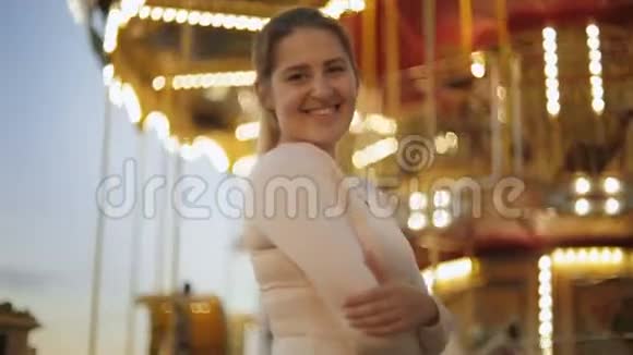 一幅美丽的微笑女子站在游乐园的明亮旋转木马旁的画像视频的预览图
