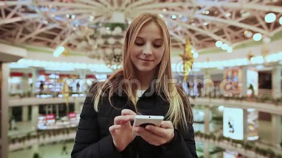 可爱的小女孩在一个大型购物中心的大楼里从手机上拿起一条信息视频的预览图