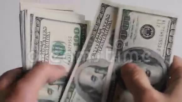 一个商人的特写他的手在一张桌子上数着一百美元的钞票视频的预览图