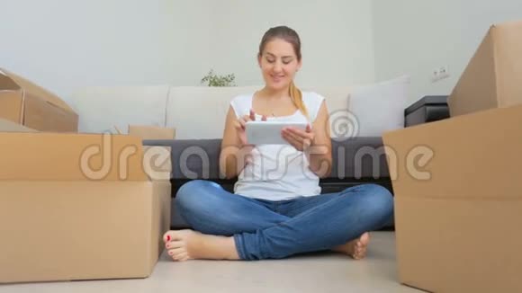 快乐的年轻女子用纸板箱包装物品并使用数字平板电脑的多莉照片视频的预览图