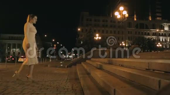 晚上穿着裙子和高跟鞋走在街上的石头楼梯上的女人视频的预览图