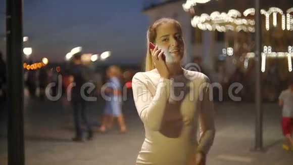 一幅美丽微笑的女人在街上晚上通过电话交谈的画像视频的预览图