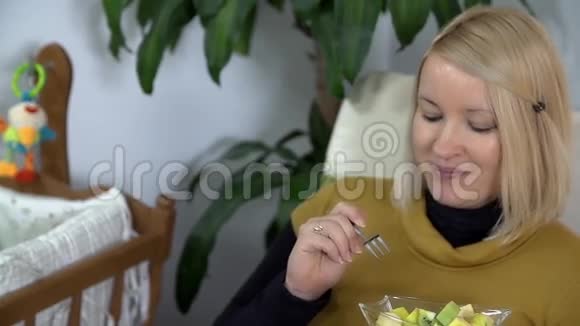 怀孕的金发女人一边吃不同的水果一边抚摸她的腹部视频的预览图