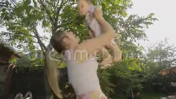 快乐的年轻妈妈抱着她的小儿子高高地站在果园里视频的预览图