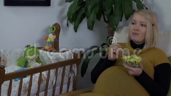 孕妇坐在婴儿床旁边吃水果杯视频的预览图