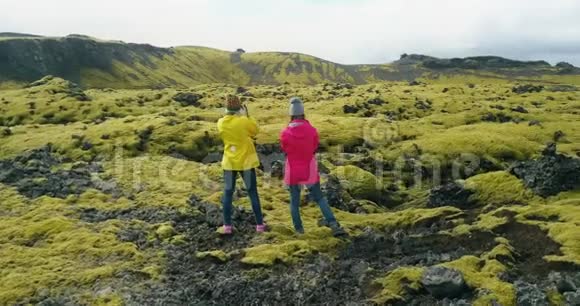 两名妇女站在冰岛的熔岩场上欣赏风景徒步旅行后的游客视频的预览图